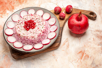 Obraz na płótnie Canvas Side view of delicious salad with various ingredients on wooden cutting board and radish with pomegranate on mixed color background