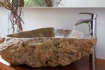 Water running from bathroom tap into original stone washbasin with decoration branches on glass...
