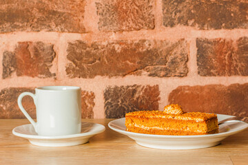 cup of coffee and cake on saucers on a wooden table against a brick wall