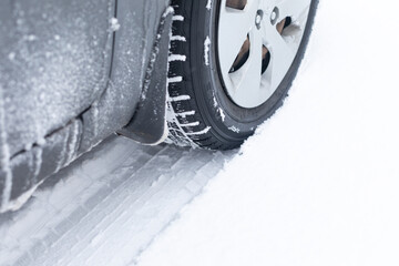 All terrain tire in snow. Snow track visible in snow with a rubber car or SUV tire in front. Tread marks in snow. Winter road safety concept.