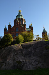 Fototapeta na wymiar Uspenski Cathedral in Helsinki, Finland, seen behind a rock and bushes