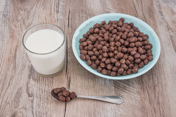 chocolate cereals in bowl and milk on wooden table.