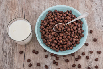 chocolate cereals in bowl and milk on wooden table.