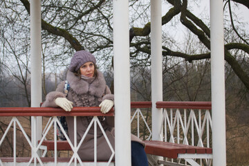 A girl in winter clothes walks in the park. Posing in the gazebo.