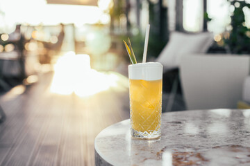 A tall glass of yellow cocktail on a sunny terrace, copy space