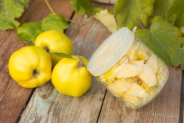 Ripe quince fruits on a wooden background. Candied quince slices in a glass jar. Conservation concept.