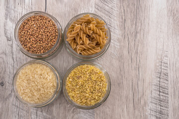 buckwheat, rice, pasta and bulgur in jars on a wooden background.