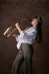 Fototapeta na wymiar girl plays jazz saxophone. talented child artist musician in a hat, shirt and trousers