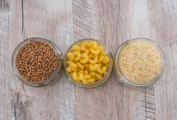buckwheat, rice, pasta in jars on a wooden background.