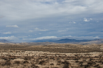 Beautiful autumn landscape with mountains, dry grass, trees and fields, unusual great sky with dark gray clouds