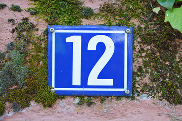 A blue house number plaque, showing the number twelve (12)