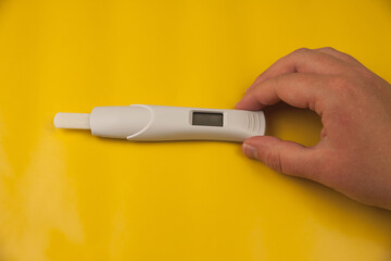 A woman's hand on a yellow background holding a pregnancy test