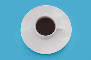 white cup of coffee in a white plate isolated on a blue background.