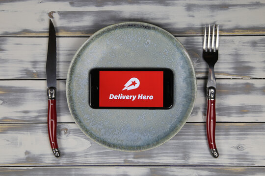 Viersen, Germany - May 9. 2020: Close up of mobile phone screen with logo lettering of food delivery service hero on wood table with dish and cutlery (focus on center)