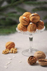 Nuts biscuits stuffed with boiled condensed milk.  Next to the vase are walnuts in shell and without shell.  Fir branches in the background. Vertical frame orientation