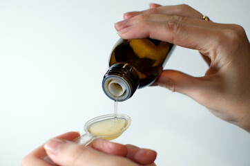 Close-up of female hands holding a bottle of expectorant cough syrup and pouring it with a...
