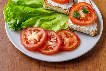 Fototapeta na wymiar dried diet bread with curd cheese, tomatoes and lettuce on a ceramic plate