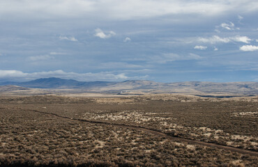 Beautiful autumn landscape with mountains on the horizon, dry grass, trees, roads, gardens, and fields, unusual great blue sky with  fluffy light gray clouds