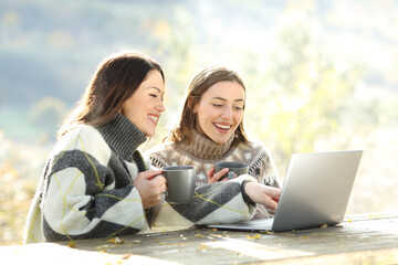 Two happy friends using laptop in winter in a park