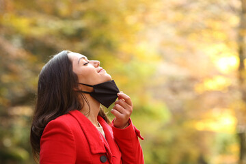 Woman taking off mask to breath fresh air in a park