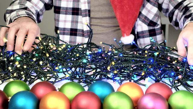 Male hands trying to prepare xmas unravel the tangled glowing lights of Decorative Christmas garland at home.
