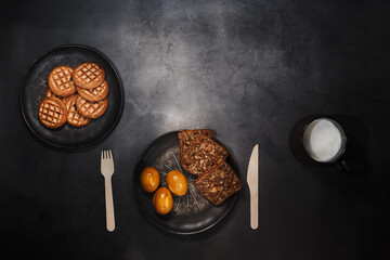 Smoked chicken eggs and bread on a plate on a dark background. wooden disposable cutlery fork and knife. A mug of milk. Fresh cookies on a plate. Dark Wood Photography. The view from the top