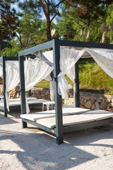 A place to relax on the beach of a Turkish resort. Sun beds with a canopy and a thin transparent fabric. Bungalow by the sea.