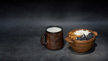 ceramic bowl with cottage cheese decorated with nuts and raisins, a mug with milk on a dark background. Still-life. The Style is rustic. copy space