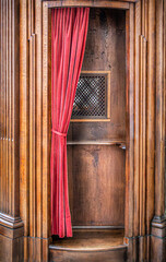 wooden confessional with red velvet curtain
