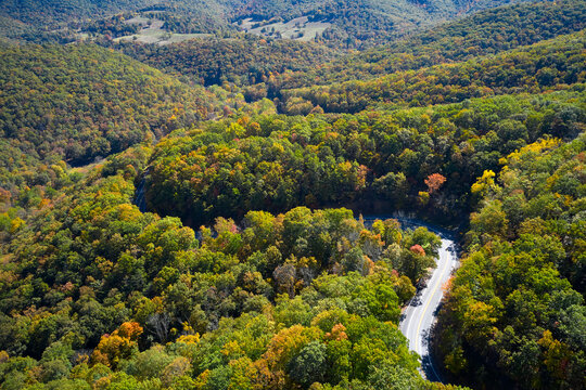 Aerial view of asphalt road winding through alpine forest in autumn