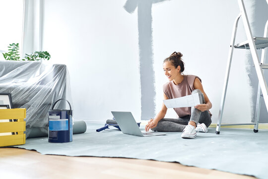 Smiling woman sitting on floor while working on laptop at home