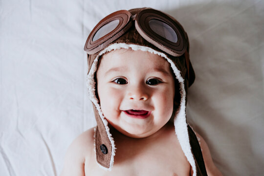 Cute male toddle wearing aviator cap while lying down on bed at home