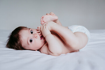 Cute baby boy putting foot in mouth while lying on bed at home