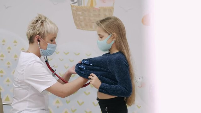 Cute preschool child standing in front of woman pediatrician listening to her heartbeat with stethoscope.