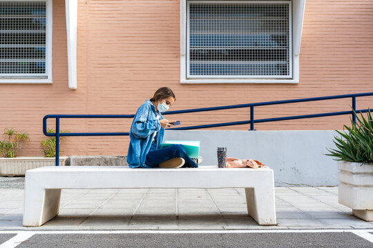 Teenage girl taking picture of notes while sitting on concrete bench
