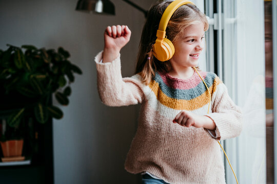 Girl wearing headphones dancing while standing by window at home