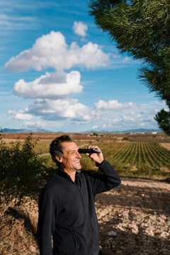 Smiling winemaker looking through refractometer at vineyard