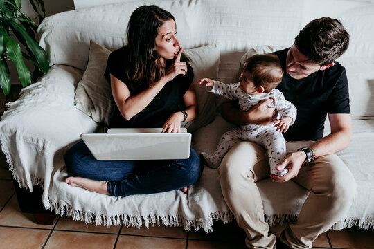 Son sitting on father's lap while mother working on laptop at home