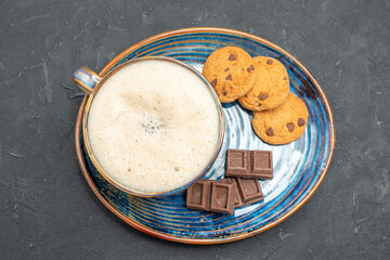 Top view of delicious breakfast with a cup of milk biscuits and chocolate bars on blue tray on dark background