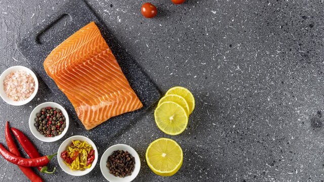 Raw salmon fillet and ingredients for cooking, seasonings and herbs on a dark background.  Stop motion animation, top view.