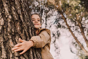 Smiling cute girl hugging tree while looking away at park