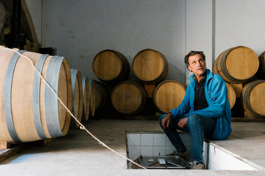Mature male worker sitting amidst barrels at winery