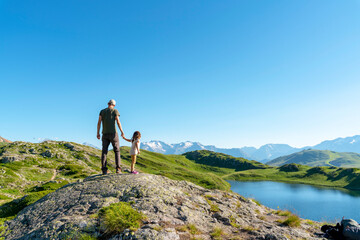 Father and daughter standing on rock object looking at view against clear sky