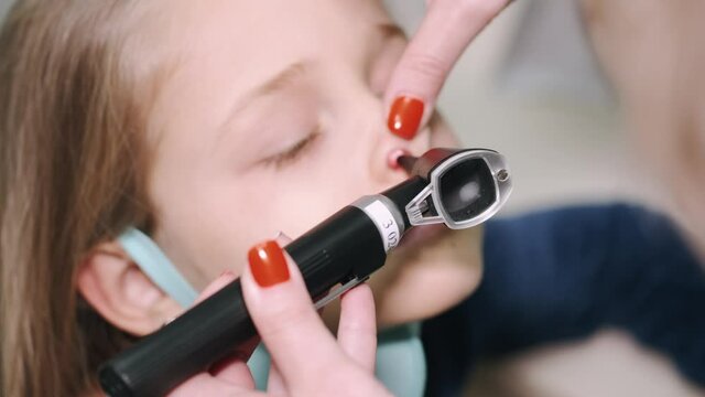 Female pediatrician checking nose of young girl in clinic exam room. Woman doctor giving exam using otoscope to child in pediatrician office. Slow motion 4k
