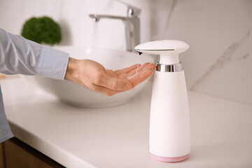 Man using automatic soap dispenser in bathroom, closeup