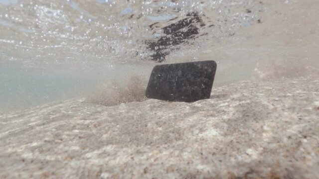 man drops phone into water and smartphone falls on sandy bottom of sea.