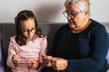 Grandmother teaches her little granddaughter how to sew.