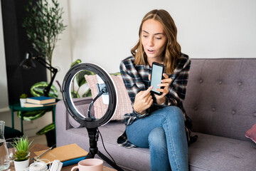 Young woman with mobile phone talking while live streaming at home