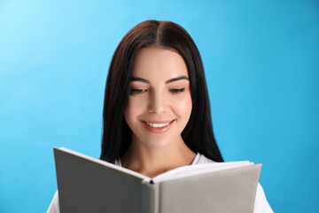 Fototapeta premium Beautiful young woman reading book on light blue background