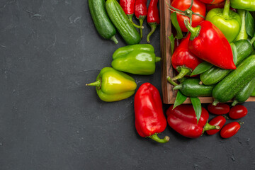Top view of fresh vegetables inside and outside of a brown wooden basket on the left side on dark background